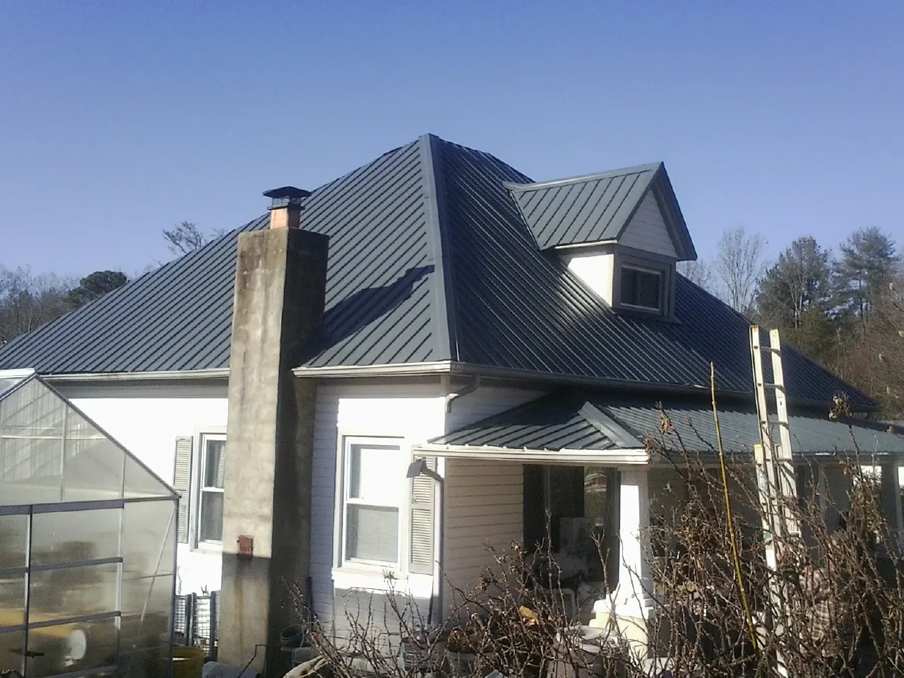 Dark blue standing seam metal roof on a white farmhouse with dormer — Slate & Tile Roof Repair by Roofing Brothers in Holloway