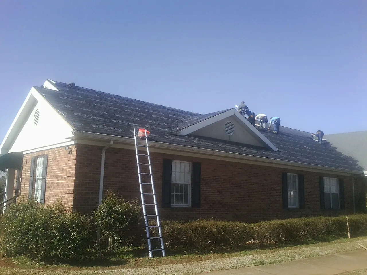 Crew tearing shingles off a brick ranch roof with a ladder set — Emergency Roof Repair work by our crew in Holloway