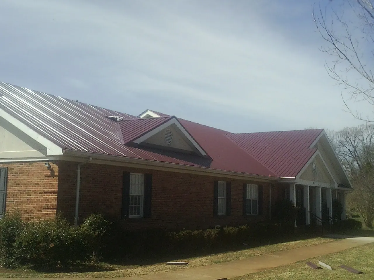 Red metal roof with gabled entries on a long brick building, from a Hail Damage Roof Repair job in Holloway