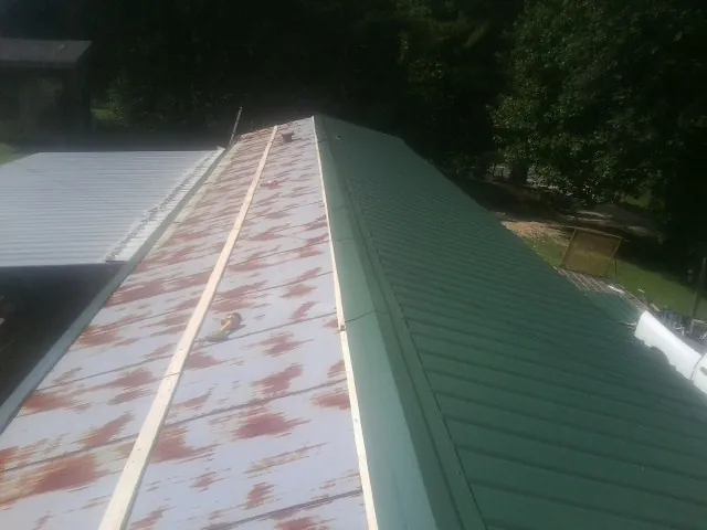 Old rusted panels beside newly installed green metal roofing — Wind Damage Roof Repair by Roofing Brothers in Holloway