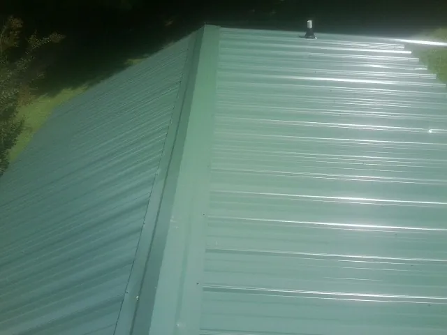 New green metal panels meeting at the ridge of a roof — Flat Roof Repair work by our crew in Holloway