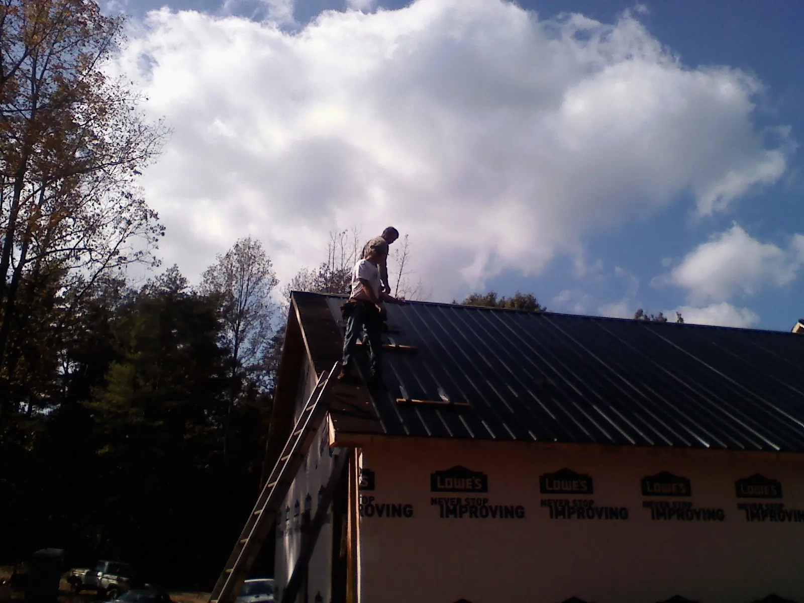 Roofer fastening dark metal panels high against a cloudy sky, from a Roof Inspection job in Holloway