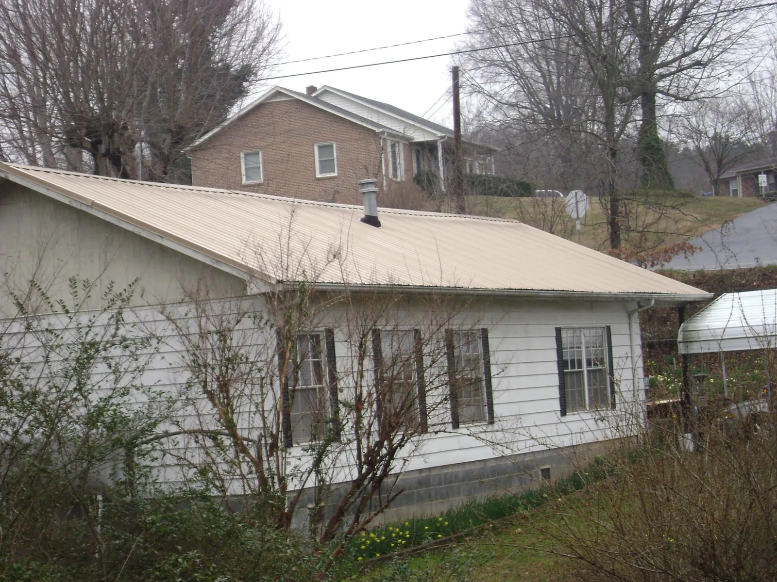 Tan metal roof on a white sided house set into a hillside — Commercial Roofing by Roofing Brothers in Holloway