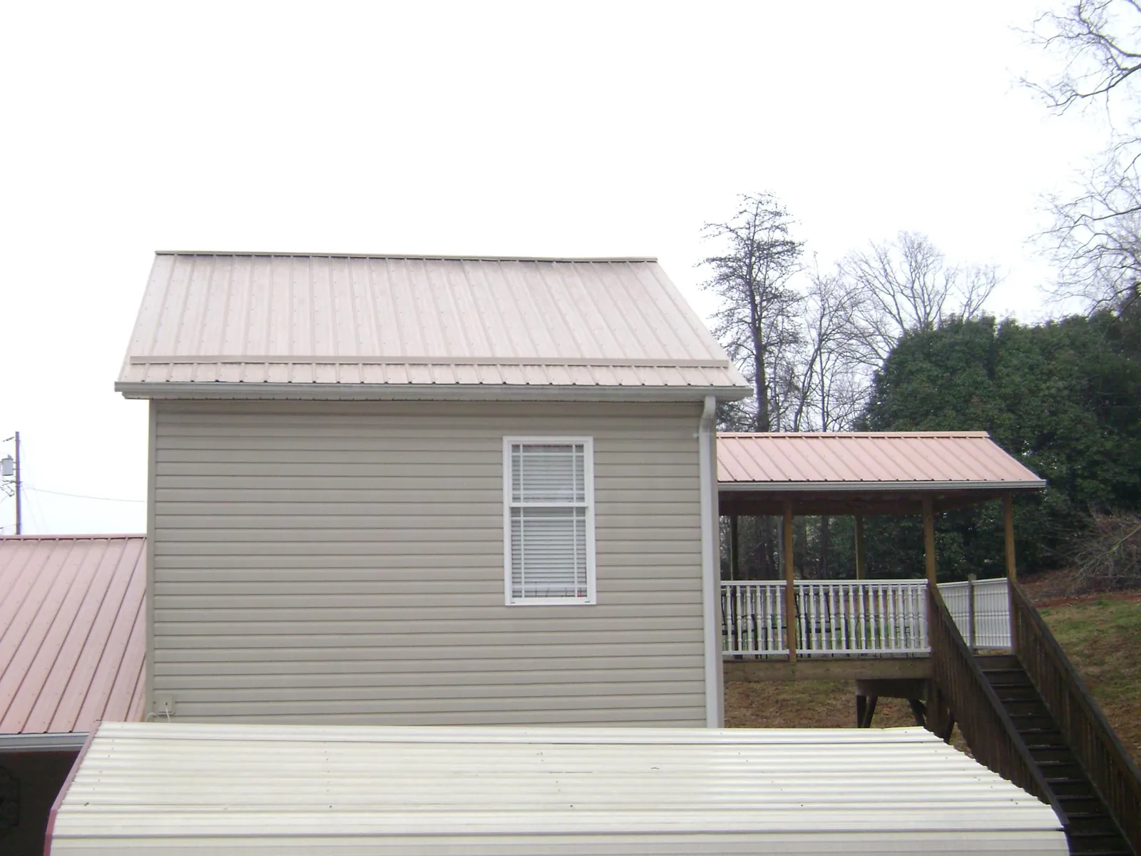 Tan metal roofs on a two story addition and attached porch, from a Roof Replacement job in Holloway